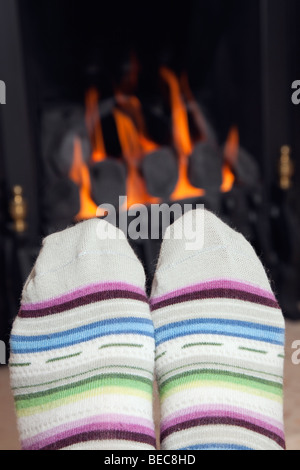 Einer Frau, die Füße in ein paar Stripy warme Wollsocken Erwärmung vor einem gemütlichen Kohle Gas Feuer mit heißen Kohlen zu Hause im Winter. England Großbritannien Großbritannien Stockfoto