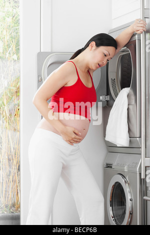 Schwangere Frau sah müde vor einer Waschmaschine Stockfoto