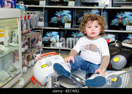 Baby Junge sitzt auf einem Einkaufswagen im Supermarkt Stockfoto