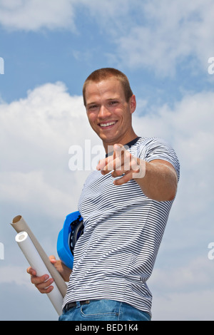 lächelnde junge Architekten mit einem Schutzhelm und Baupläne Stockfoto