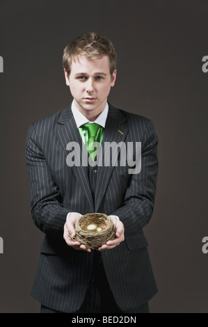 Geschäftsmann hält ein goldenes Ei in einem nest Stockfoto