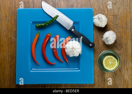 Frische rote und grüne Peperonccini, japanische Messer, blaue Platte Stockfoto