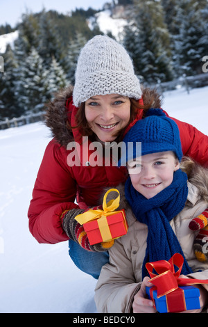 Frau und Mädchen kniend im Schnee, mit Geschenken, lächelnd Stockfoto