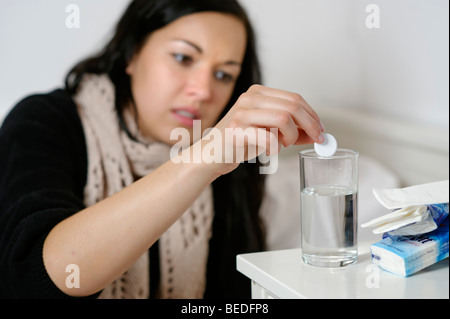 Junge Frau wirft ein Aspirin in ein Glas Wasser, hat einen Husten, Erkältung, Grippe, krank Stockfoto