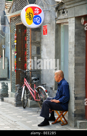 Alte Mann sitzt vor einem Hauseingang an Qiwachang Hutong Beijing, CN Stockfoto