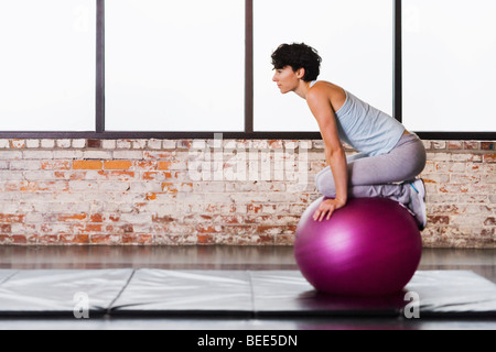 Eine junge Frau auf einem Gymnastikball kniend darauf balancieren. Stockfoto