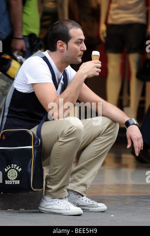 Junger Mann männliche Touristen sitzen auf dem Bürgersteig Bürgersteig Essen ein Eis Eis in Piazza del Duomo Mailand Italien Stockfoto