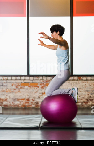 Eine junge Frau auf einem Gymnastikball kniend darauf balancieren. Stockfoto