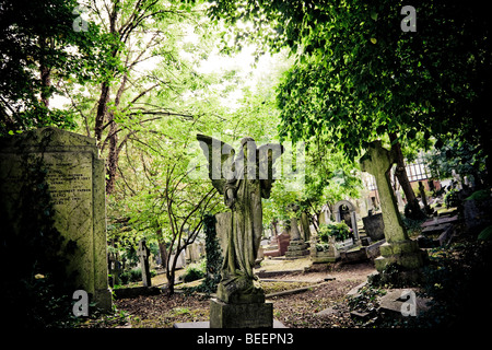 Ein Stein Engel gestalteten Grabstein steht über einem Grab zwischen Bäumen in Highgate Cemetery North London England UK Stockfoto