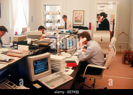 Unternehmerinnen und Unternehmer beschäftigt sprechen auf Handys mit dem Computer auf Desktop-PCs in kleinen Börsenmakler Büro in Stockholm Schweden Stockfoto