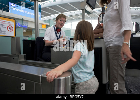 Junges Mädchen im Chat mit kinderfreundlichen British Airways Check-in-Dame am Flughafen Heathrow Terminal 5. Stockfoto