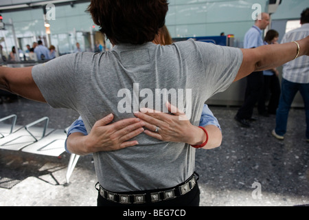 Weibliche operative Sicherheit fühlt sich um einen männlichen Passagier zurück nach verdächtigen Elementen während der Suche am Flughafen Heathrow T5 Stockfoto