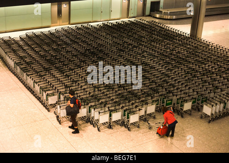 Flugpassagiere sammeln Trolleys in der Gepäckhalle Rückforderung in der Ankunftshalle des Flughafens Heathrow Terminal 5. Stockfoto