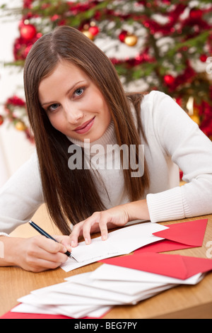 Junge Frau denken während des Schreibens Weihnachtskarte vor Baum Stockfoto