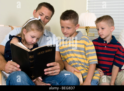 Ein Vater liest seine drei kleinen Kinder aus der Bibel. Stockfoto