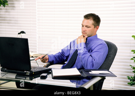 Eine junge attraktive Geschäftsmann sitzt an seinem Schreibtisch tief in etwas darüber nachgedacht. Stockfoto