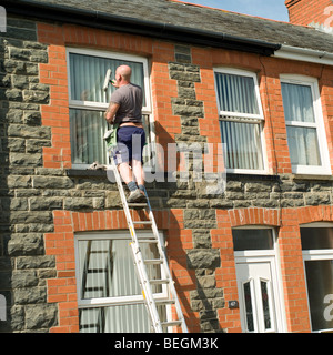 Selbständiger Einzelunternehmer Mann stehend auf Leiter Fensterputzen ein Reihenhaus, Aberystwyth Wales UK Stockfoto