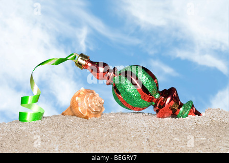 Eine schöne Weihnachten ornament mit grünen Band an einem Sandstrand und vor blauem Himmel mit weißen geschwollenen Wolken bereit. Stockfoto