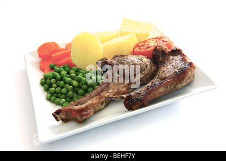 Kraut adobado Gegrillte Lammkoteletts serviert mit gekochten Kartoffeln, in Scheiben geschnittene Karotten und Erbsen auf einem weißen Teller mit einem Schatten. Stockfoto