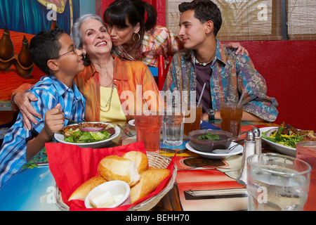 Reife Frau küssen ihre Mutter mit ihren zwei Kindern sitzen an einem Tisch in einem restaurant Stockfoto