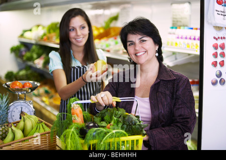 Porträt einer Reife Frau mit einem Warenkorb und eine weibliche Verkäuferin, indem er ihr eine mango Stockfoto