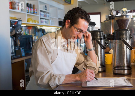 Männliche Verkäuferin mit einem schnurlosen Telefon und Inventar überprüfen Stockfoto