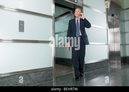 Unternehmer im Gespräch auf ein Mobiltelefon in einem Korridor Stockfoto
