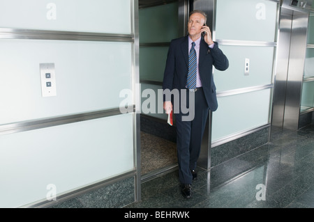 Unternehmer im Gespräch auf ein Mobiltelefon in einem Korridor Stockfoto