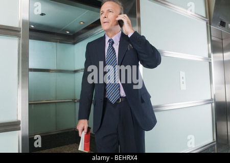 Unternehmer im Gespräch auf ein Mobiltelefon in einem Korridor Stockfoto