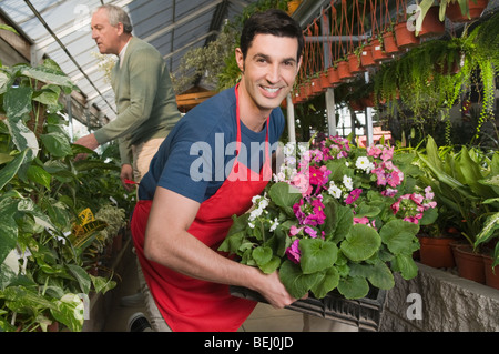 Mann, der eine Kiste von Pflanzen in einem Garten-Center mit einem Kunden im Hintergrund hält Stockfoto