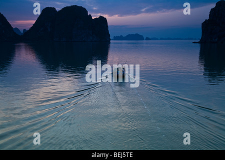 Einsamer Bootstouren durch das Wasser in der Dämmerung auf Halong Bucht, Vietnam. Stockfoto