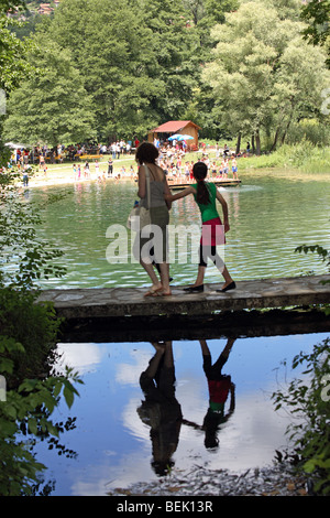 Menschen überqueren Fußgängerbrücke. Spiegelungen im Wasser unter. Pliva Seen, Jajce, Bosnien und Herzegowina, Balkan. Stockfoto