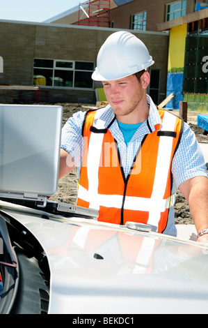 Männliche Bauingenieur Sachverständiger Architekt mit einem Laptop auf einer Baustelle tragen Sicherheit Hi Vis Weste und Helm Stockfoto