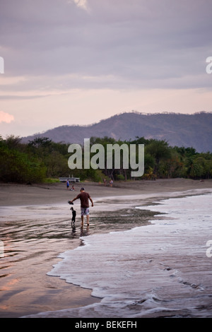 Mann zu Fuß und spielen mit seinem Hund am Strand in der Abenddämmerung in Playa del Coco, Provinz Guanacaste, Costa Rica. Stockfoto