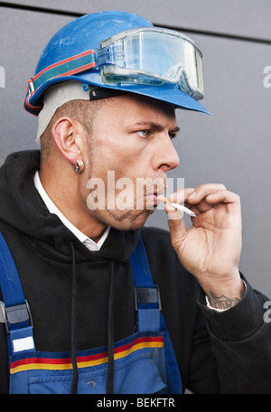 Arbeiter in Schutzkleidung und einen blauen Helm Rauchen im freien Stockfoto