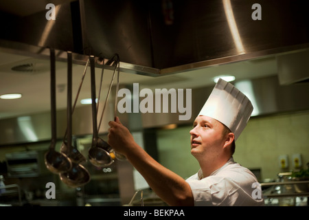 Ein Koch einen traditionellen Mütze Hut greift nach einer Kelle im Hotel-Restaurant-Küche. Stockfoto