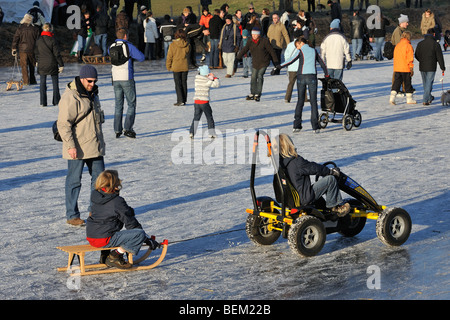 Kind auf Schlitten gezogen von Go-Kart unter Eisläufer Schlittschuhlaufen auf dem Eis der zugefrorenen Fluss im winter Stockfoto