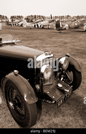 Aston Martin Mk2 1934 auf dem Flugplatz bei Goodwood Revival Meeting, Sussex, UK. Mustangs und Spitfire im Hintergrund. Stockfoto