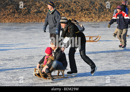 Mutter und Sohn auf Schlitten von Vater und Schlittschuhlaufen auf zugefrorenen Fluss im Winter Eisläufer geschoben Stockfoto