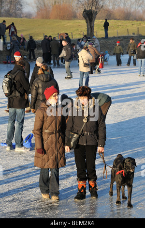 Wanderer mit Hund an der Leine unter Eisläufer auf dem zugefrorenen Kanal in Damme im Winter, West-Flandern, Belgien Stockfoto