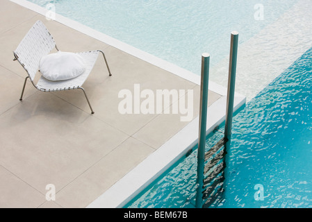 Stuhl mit Kissen am Rand des Pools in der Nähe von Leiter Stockfoto