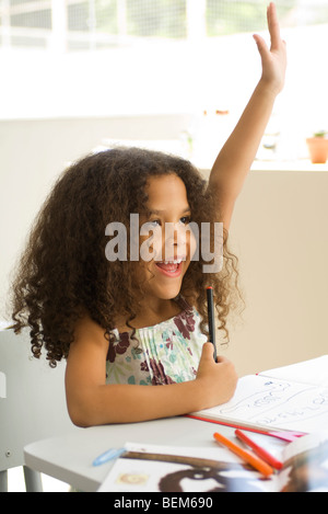 Kleines Mädchen sitzt am Schreibtisch, hob die Hand mit Begeisterung Stockfoto