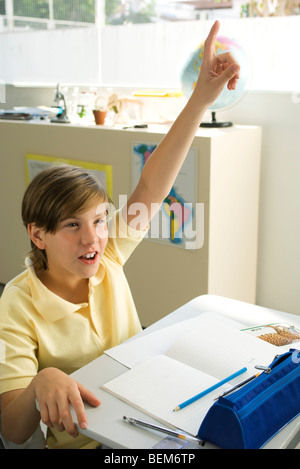 Junge sitzt im Klassenzimmer, hob die Hand mit Begeisterung Stockfoto