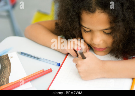 Kleines Mädchen auf Schreibtisch, Kopf ruht auf Karopapier zeichnen Stockfoto
