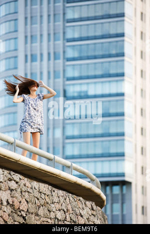 Junge Frau, die auf Balkon, langes Haar über Gesicht weht wind Stockfoto