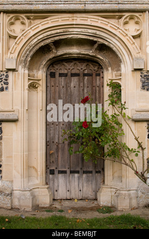 Eine sehr alte Holztür in der reich verzierten Tür der Kirche St. Peter und St. Paul in Cavendish, Suffolk, England. Stockfoto