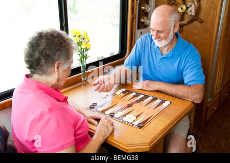 Älteres Paar im Urlaub spielen Backgammon in ihrem Wohnmobil. Bewegungsunschärfe auf die Hand des Mannes, wie er die Würfel schüttelt. Stockfoto