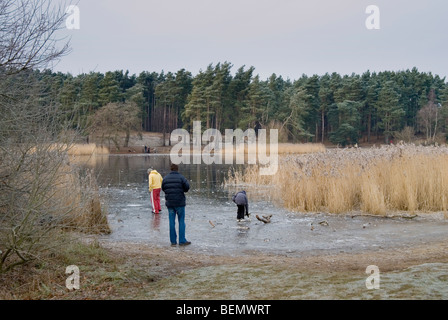 Frensham Teiche im Winter mit dem See zugefroren und Menschen neben dem See und spielen auf dem Eis Stockfoto