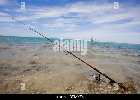 Angelrute Setup entlang des Strandes, während ein Fischer seinen Fang im Meer sucht. Stockfoto