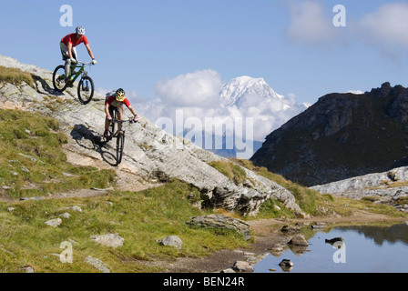 Zwei Mountainbiker fahren einen felsigen Hang an einem See in den Bergen in der Nähe von Les Arcs in den französischen Alpen. Stockfoto